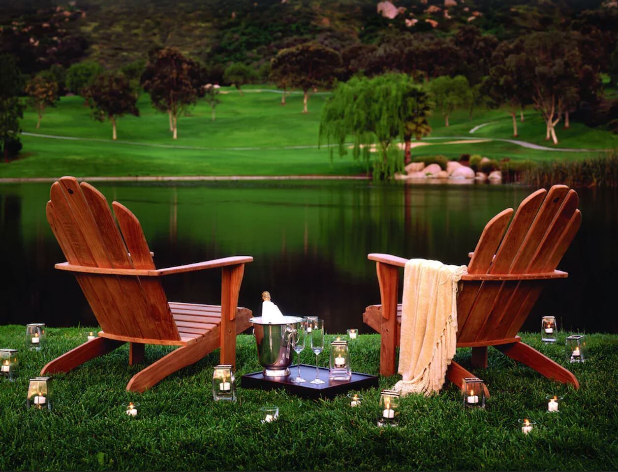 Deux fauteuils Adirondack en bois, placés face à un plan d’eau, avec un terrain de golf en arrière-plan.