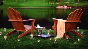 Dos sillas Adirondack de madera mirando un cuerpo de agua, con un campo de golf al fondo.