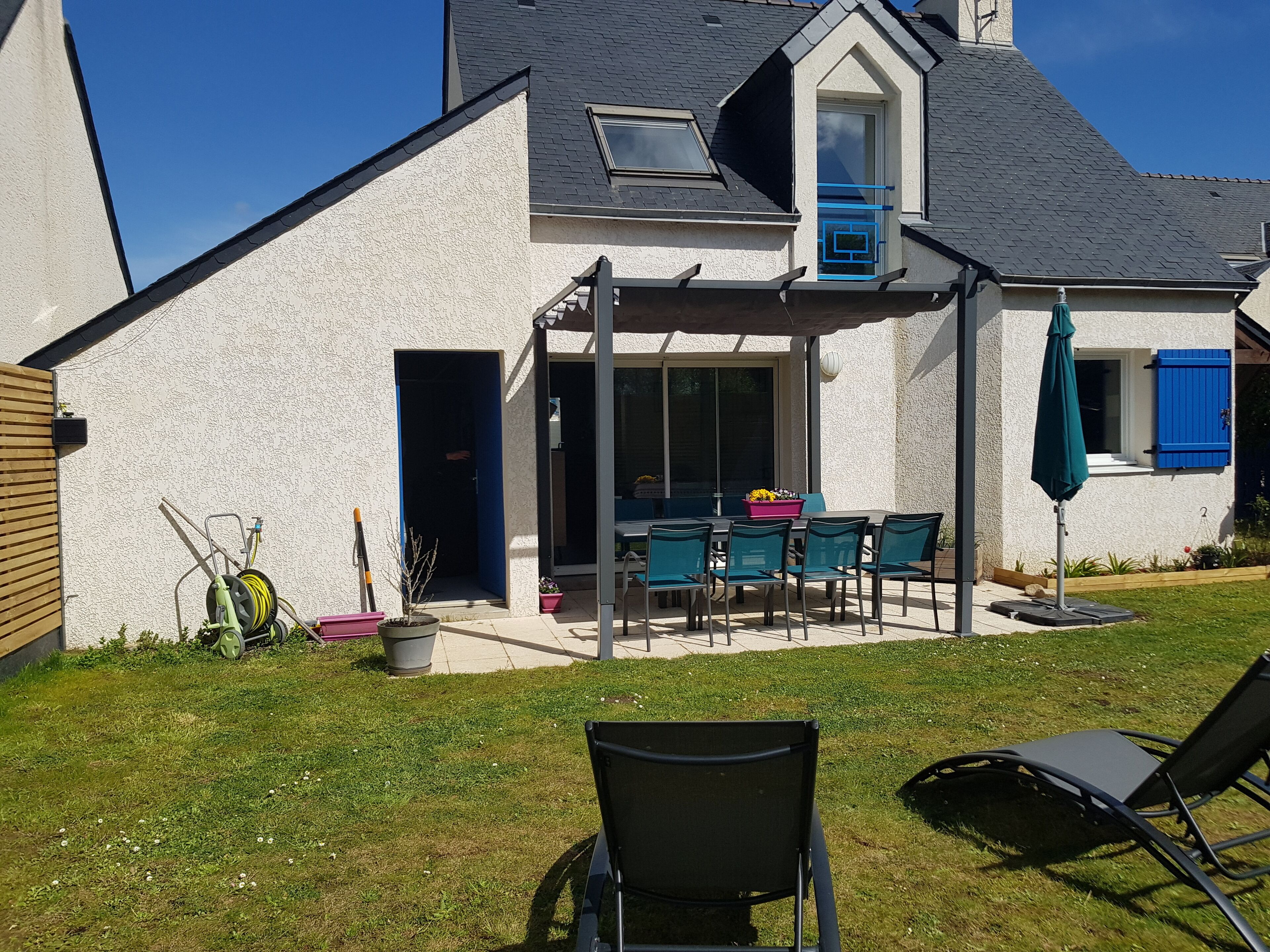 Una casa con un patio que incluye una mesa y sillas, una zona de estar cubierta y un pequeño jardín.