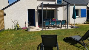 Una casa con un patio que incluye una mesa y sillas, una zona de estar cubierta y un pequeño jardín.
