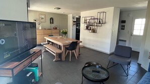 Una sala moderna con un televisor de pantalla plana, una mesa de comedor con sillas, una mesita de centro y un sofá.