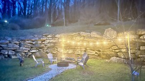 A stone wall with string lights, a fire pit, and outdoor seating. - Mountain Laurel Cottage ~ Bat Cave North Carolina  RELAX, REFRESH, RENEW! (Hendersonville)