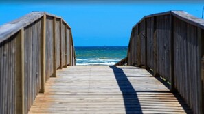 Une promenade en bois qui mène à l’océan, offrant une vue dégagée sur la mer et le ciel.