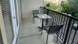 Un balcón con mesa y sillas, vista a un edificio y una zona con césped.