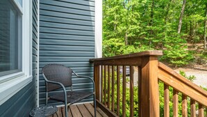 A wooden deck with a metal chair and a small table, overlooking a forested area. - Cedar Blossom Bungalow - Pet friendly getaway with a 5 min walk to downtown (Hot Springs)