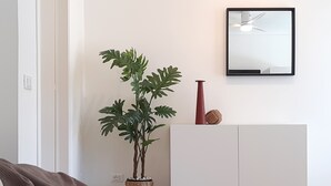 Un salon avec un canapé blanc, une plante en pot, un vase rouge et un meuble blanc.