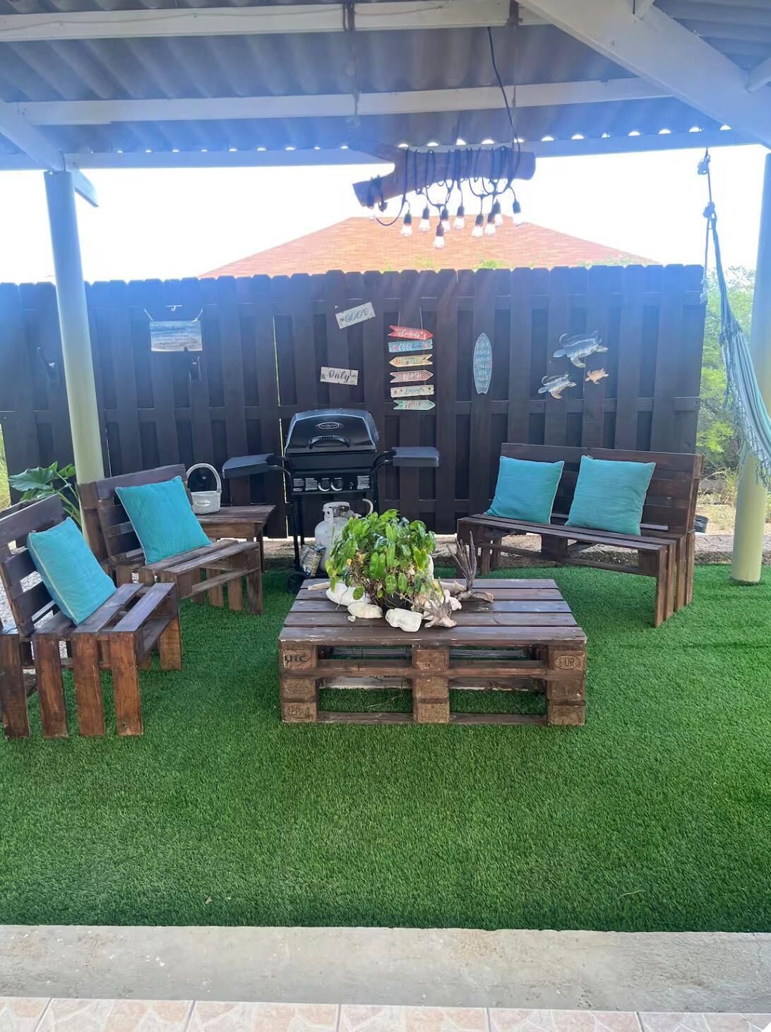 Un patio exterior con zona de estar cubierta, una parrilla de barbacoa y una hamaca.
