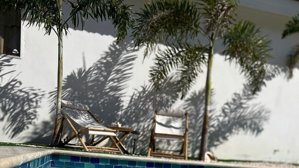 A clear swimming pool with blue tiles, surrounded by lounge chairs and palm trees. - Aruba Sun, Sand & Beach  Apartment 5 min from Beach. (Sanicolas)