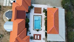 An aerial view of a property with a swimming pool, multiple rooms with orange roofs, and a patio area. - Aruba Sun, Sand & Beach  Apartment 5 min from Beach. (Sanicolas)