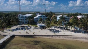 A resort with multiple buildings, a beach area with palm trees, and a clear sky. - Charming 3 Bed Condo with Exquisite Caribbean View (San Pedro Town)