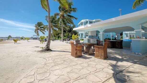 A beachfront property with a patio area featuring outdoor furniture, a pool, and a building with a light blue exterior. - Charming 3 Bed Condo with Exquisite Caribbean View (San Pedro Town)