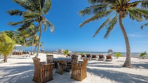 A beachside seating area with wooden chairs and tables, palm trees, and a view of the ocean. - Charming 3 Bed Condo with Exquisite Caribbean View (San Pedro Town)
