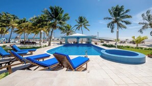 A pool area with lounge chairs and palm trees, overlooking the ocean. - Charming 3 Bed Condo with Exquisite Caribbean View (San Pedro Town)