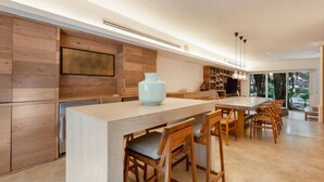 Cuina moderna amb armaris de fusta, una illa gran amb tamborets i una zona de menjador amb taula i cadires.