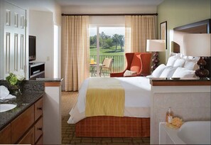 Quarto de hotel com cama, escrivaninha, cadeira, banheiro e vista para o exterior.