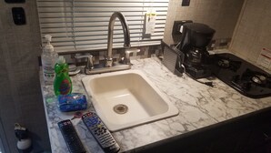 Una cocina con un lavamanos blanco, una cafetera y un dispensador de gel antibacterial.