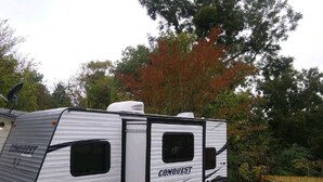 Una caravana CONQUEST RV estacionada en un patio trasero con una valla de madera y árboles al fondo.