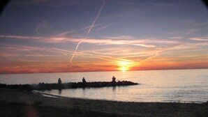 A sunset over a calm sea with a rocky outcrop in the foreground. - Welcome to Bayside Breeze! One Block From Town Beach, Walk to Waterfront Dining (Rock Hall)