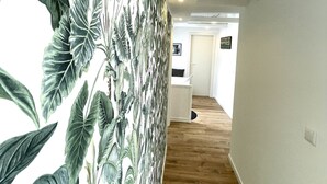 Un pasillo con un mural de hojas tropicales, piso de madera y una puerta blanca al final.