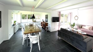 Un amplio salón con una mesa de comedor, sillas, un sofá y un televisor montado en la pared.