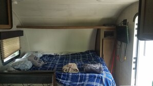 En kompakt campingvogns indretning med køjeseng, et lille bord og et tv ophængt på væggen.