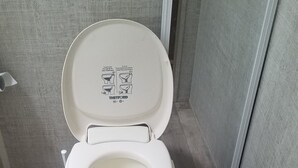 Et toilet med lukket låg, en synlig instruktionstavle og et blåt rør på gulvet.