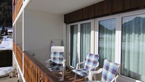 Ein Balkon mit zwei weißen Stühlen und einem weißen Tisch mit Blick auf eine verschneite Landschaft.