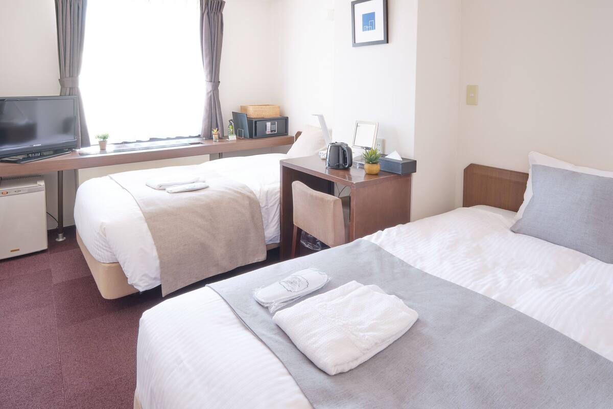 A hotel room with two beds, a desk with a computer, a television, and a window with curtains.