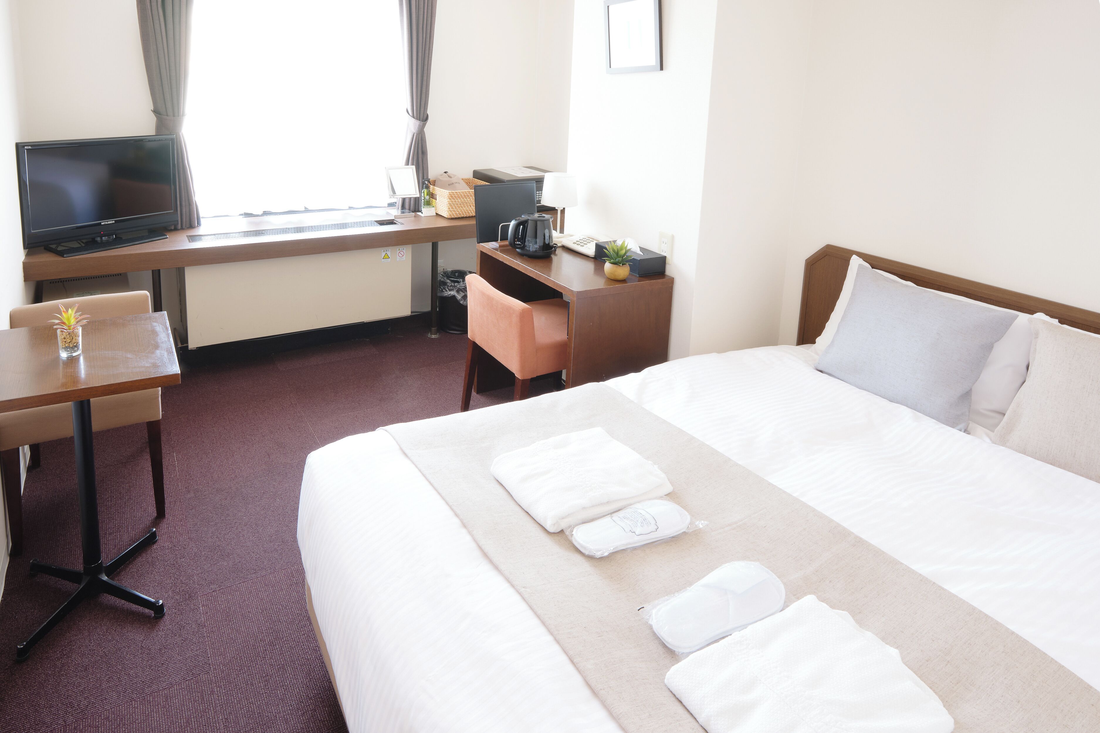 A hotel room with a bed, a desk with a computer, a television, and a window with curtains.