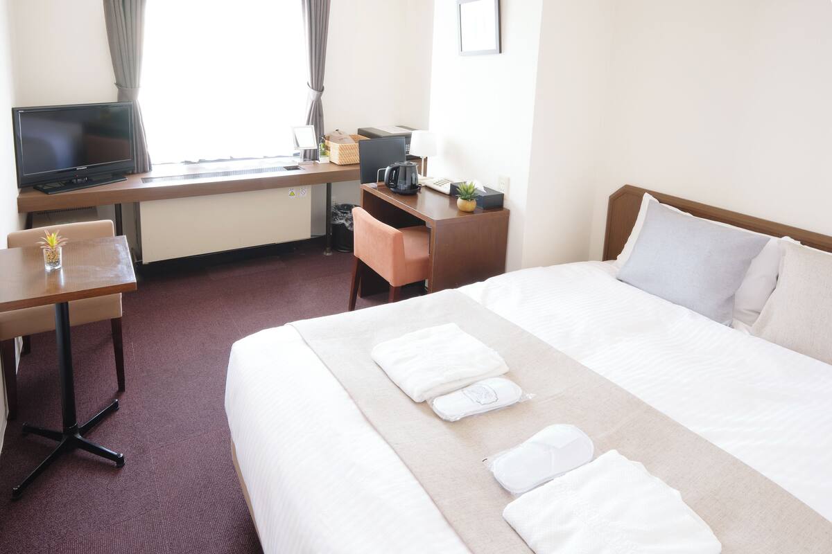 A hotel room with a bed, a desk with a computer, a television, and a window with curtains.
