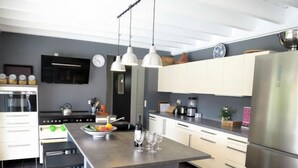 Une cuisine moderne dotée d’un îlot central, d’appareils électroménagers en acier inoxydable et de luminaires suspendus.