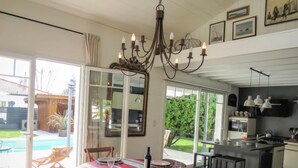Un coin repas avec une table dressée pour six personnes, un lustre et une vue sur le jardin.
