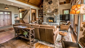 Ein rustikales Interieur mit Kamin aus Stein, Ledersofas und einer Holztreppe.