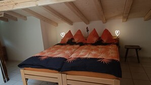 A bedroom with a wooden bed, orange and black bedding, a nightstand with a lamp, and a small stool. - Lischa 3. OG Süd by Interhome (Fiesch)