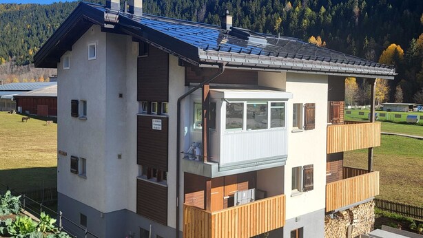 A multi-story building with a balcony, a small attached structure, and a view of a forested hillside. - Lischa 3. OG Süd by Interhome (Fiesch)