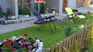 A patio with two lounge chairs, a red umbrella, and a garden with flowers and rocks. - Lischa 3. OG Süd by Interhome (Fiesch)