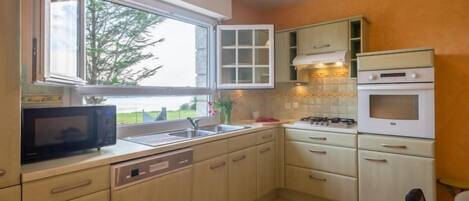 A kitchen with a window, a microwave, a sink, cabinets, a stove, and a chair.