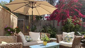 Een terras met rieten meubels, een blauwe tafel en een beige parasol.