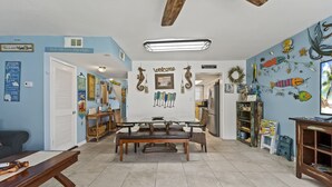 Une pièce avec une table et des chaises en bois, une pancarte « Bienvenue » et divers éléments de décoration murale, notamment des poissons et des hippocampes.