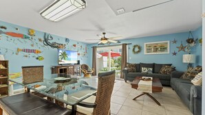 Un salon comprenant une table à manger en verre, des chaises en osier, un canapé et un ventilateur de plafond.