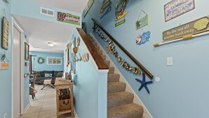 Un escalier avec une rampe en bois et des marches recouvertes d’une moquette beige, décoré d’étoiles de mer et d’œuvres d’art murales sur le thème de la marine.