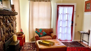 Un salon avec une cheminée en pierre, un canapé en cuir, un tapis rouge à motifs et un plancher en bois.