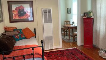 A bedroom with a bed, a red patterned rug, a red cabinet, and a small table with a chair.