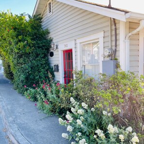 A house with a red door, number 782, surrounded by lush greenery and flowering plants. - Mary's Place is a historic cottage with private garden in the center of town. (Garberville)