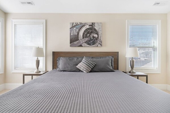 Een slaapkamer met een groot bed, twee nachtkastjes met lampen, een hoofdeinde en een kunstwerk aan de muur.