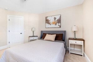 A bedroom with a large bed, two bedside tables, a door, and a wall-mounted artwork.