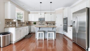 A modern kitchen with white cabinetry, stainless steel appliances, and a central island with bar stools.