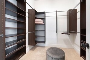 A walk-in closet with multiple shelves, a hanging rod, and a storage bench.