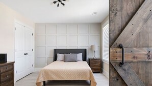A bedroom with a bed, a nightstand, a dresser, and a wooden door.