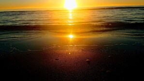 Ein Strand bei Sonnenuntergang, wobei sich die Sonne im Wasser spiegelt.